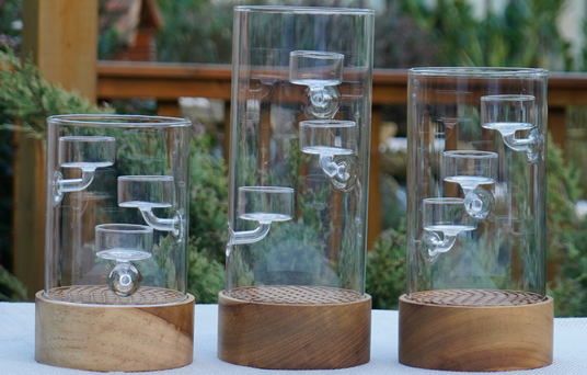 Three glass and wooden cylindrical decorative items on a table with a garden background