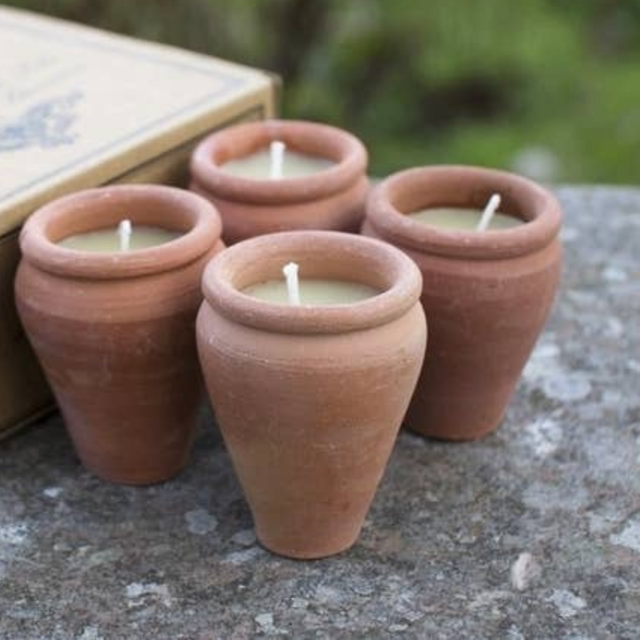 Four terracotta pots with candles on a stone surface