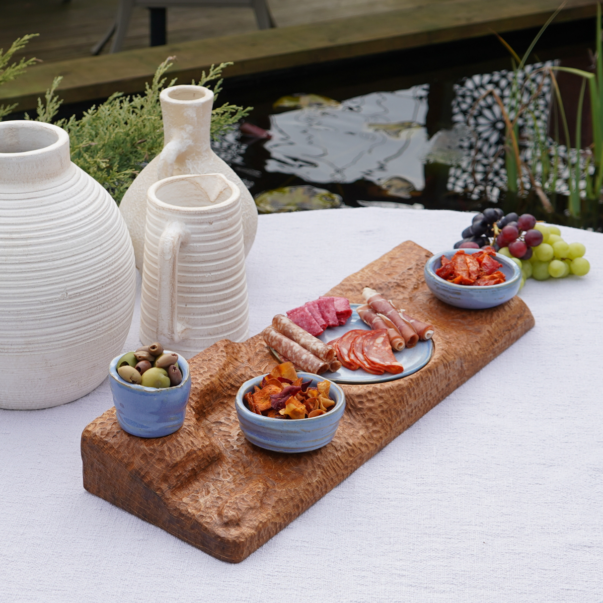 Dried fruit and nuts on a wooden board with ceramic containers and vases outdoors.