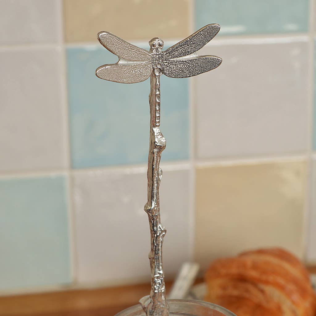 Decorative silver dragonfly on a branch with a tiled wall background