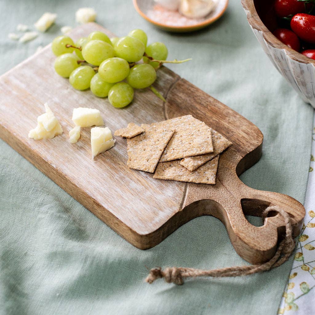 A heart-handled wooden board with cheese, crackers and grapes.