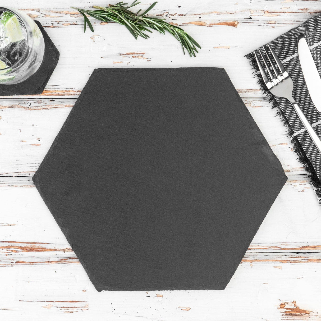 Hexagonal black placemat on a wooden table with cutlery and herbs.