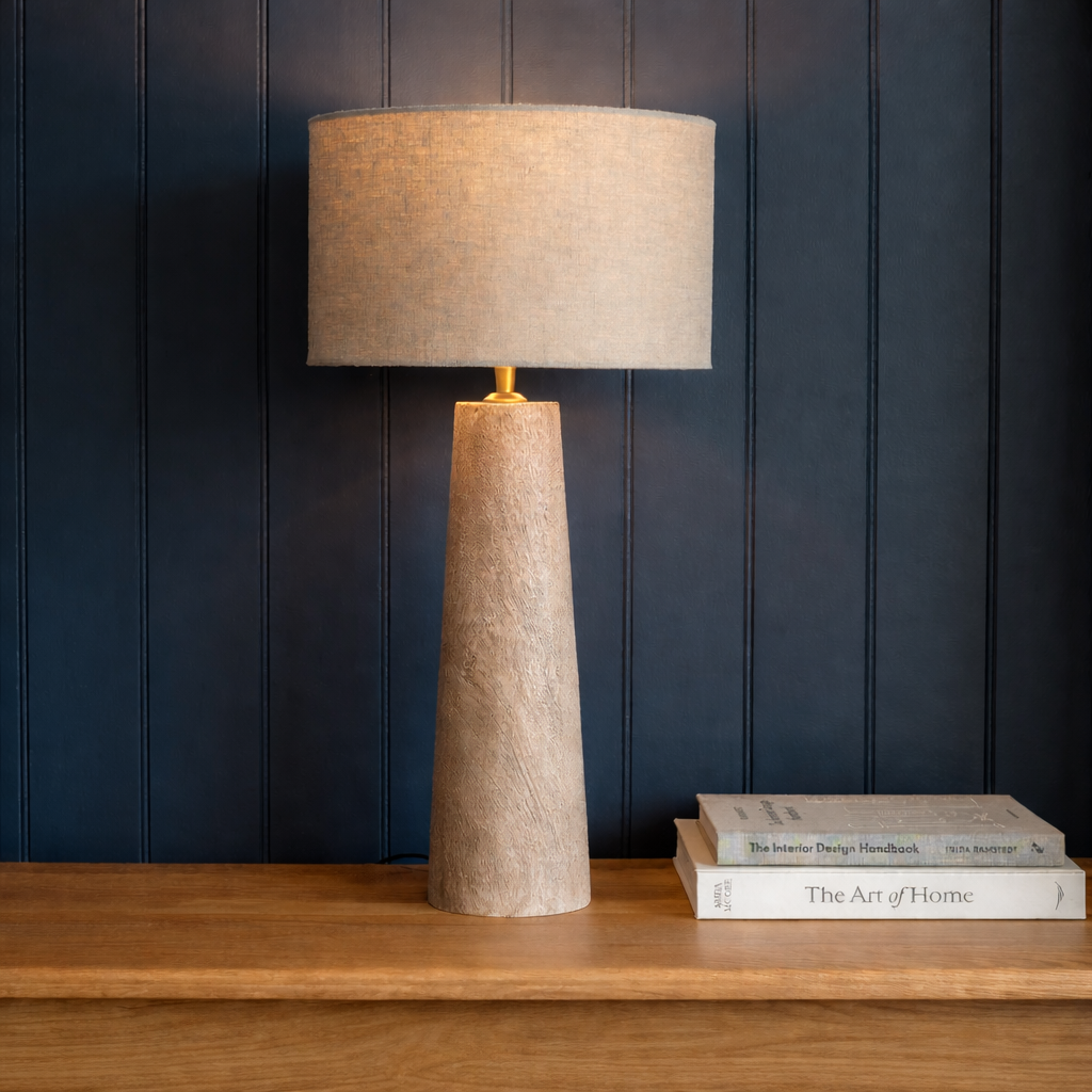 Textured table lamp on a wooden surface with books against a dark paneled wall