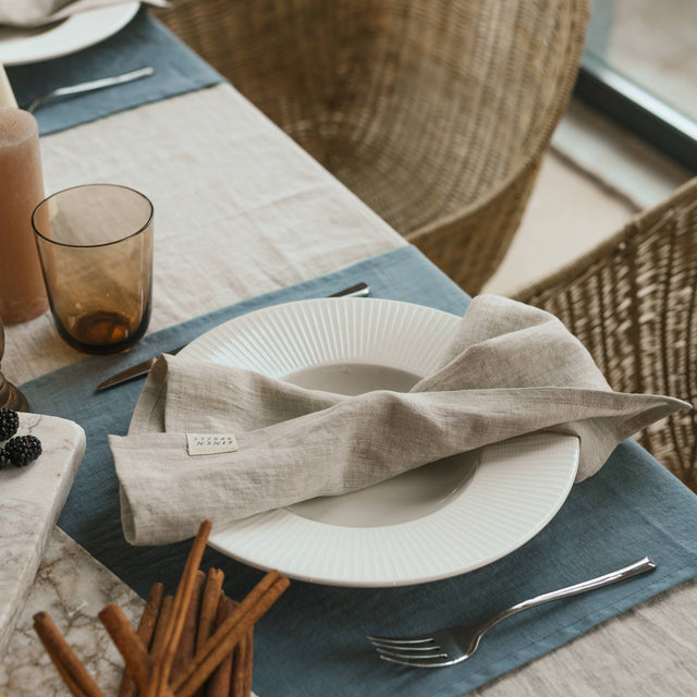 Dining table setting with a white plate, folded beige napkin, and blue placemat.