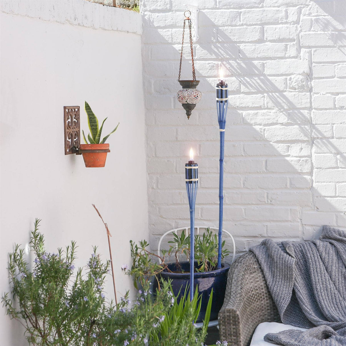 Outdoor setting with blue torches, plants, and a white brick wall.
