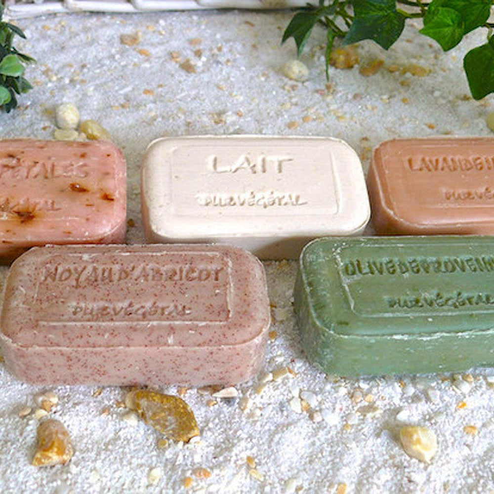 Five bars of soap in different colors on a textured surface with greenery.