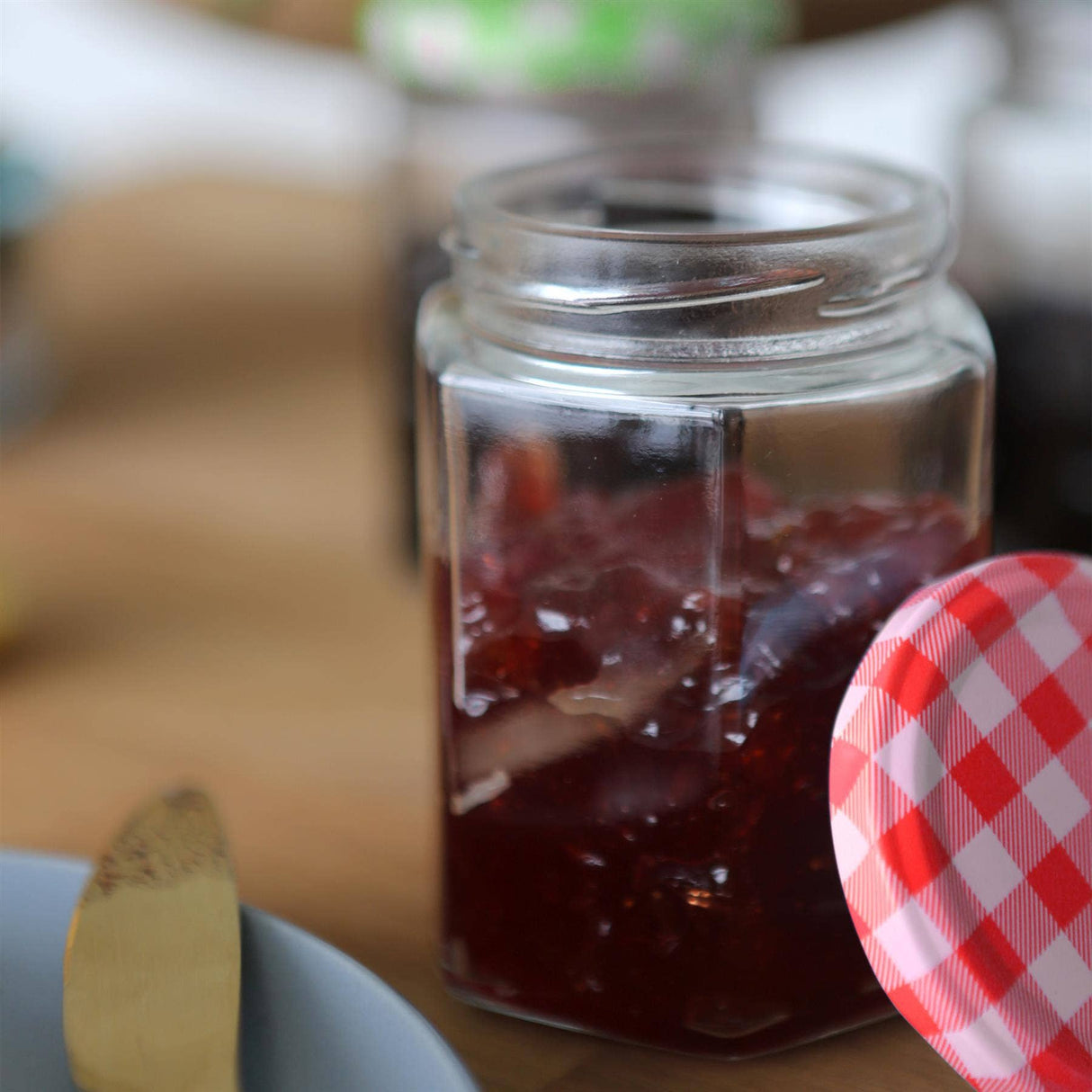Jar of red jelly with a checkered lid on a wooden surface