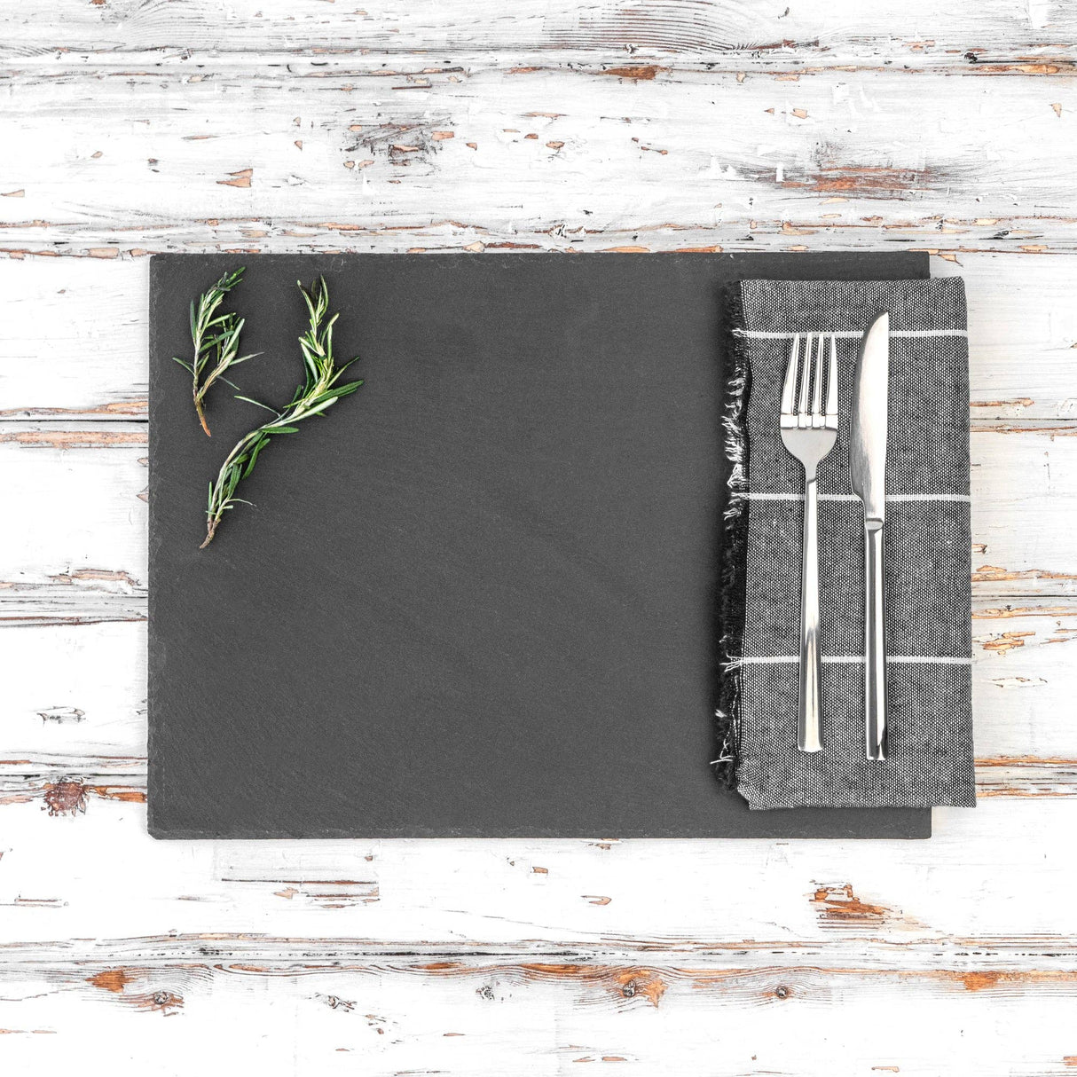 Slate platter with herbs and cutlery on a wooden surface