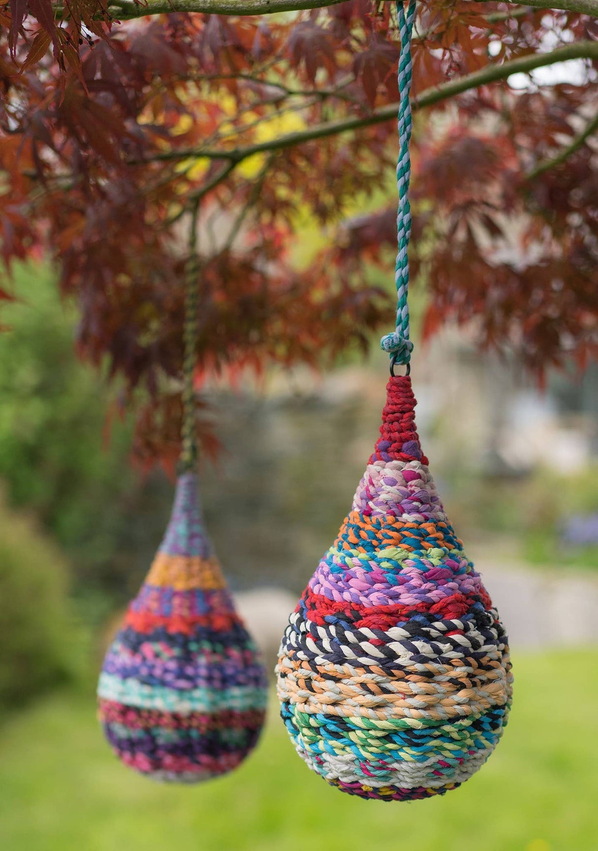 Colorful woven teardrop-shaped hanging decorations in a garden setting.