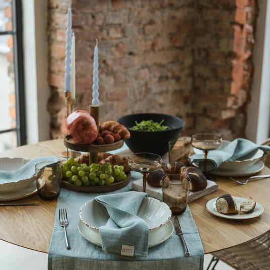 Dining table set with plates, glasses, and a fruit platter against a brick wall.