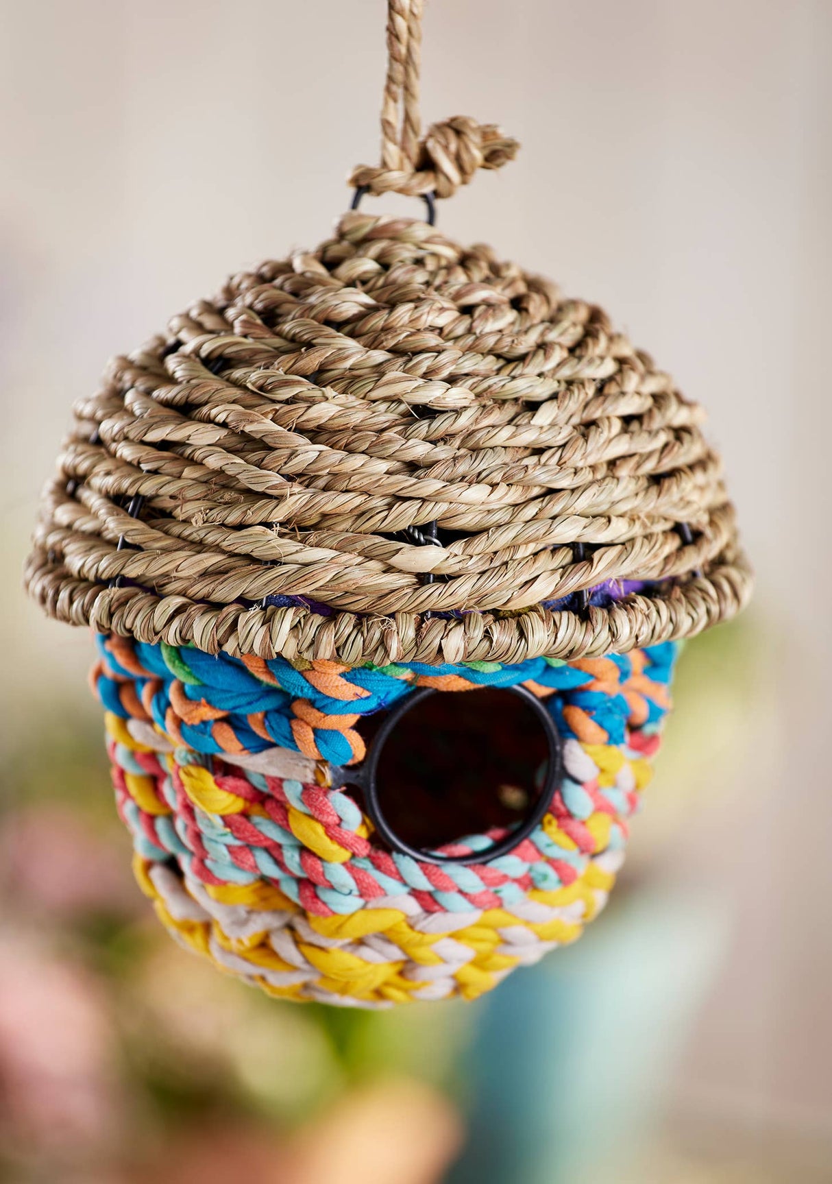 Colorful woven birdhouse with rope top on a blurred background