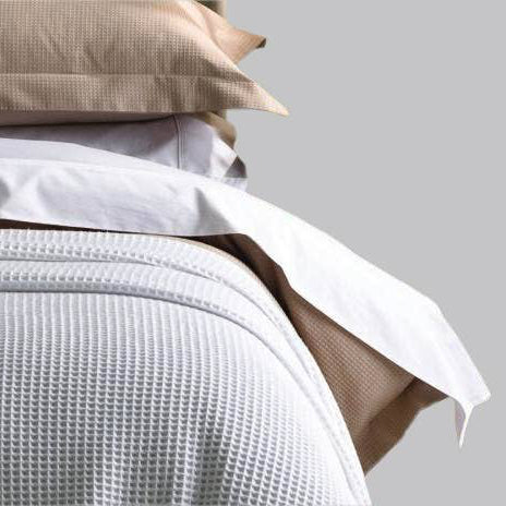 Neatly made bed with white bedding and a decorative pillow on a neutral background