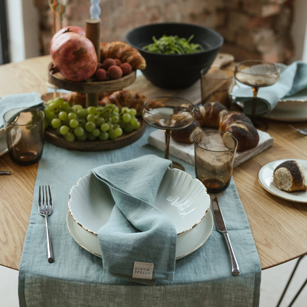 Dining table setting with plates, napkins, and fruit on a wooden table.