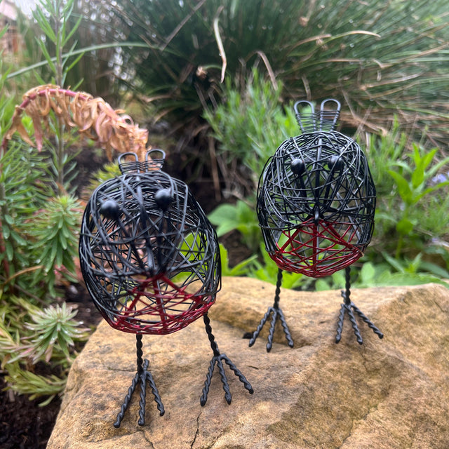 Two wire bird sculptures on a rock with greenery in the background