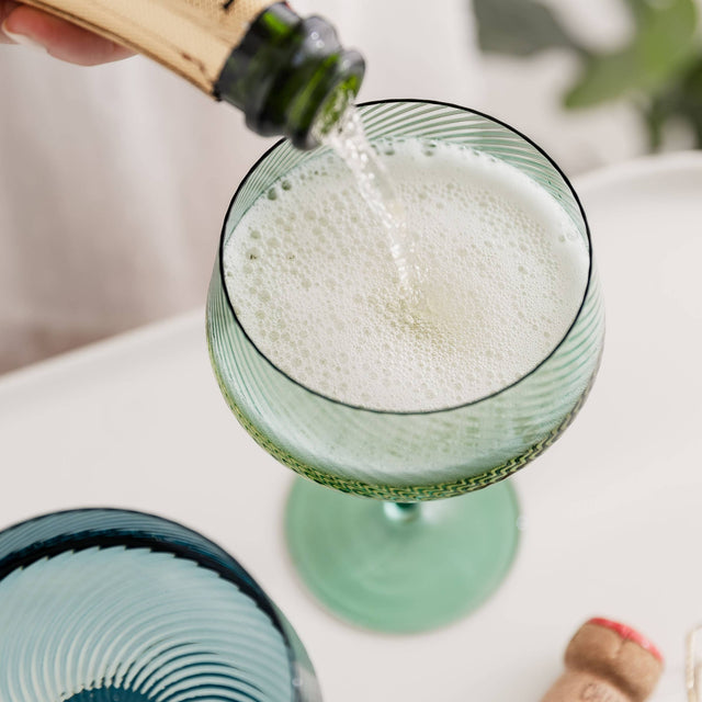 Green glass being filled with a bubbly beverage from a champagne bottle.
