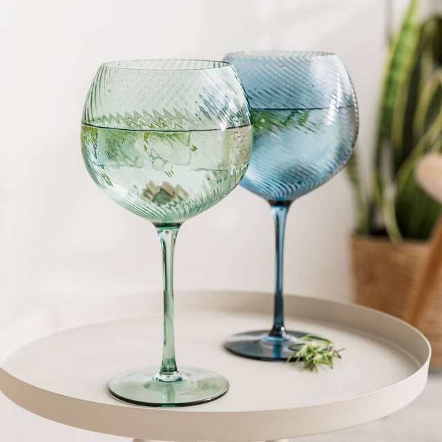 Two textured wine glasses on a round white surface with a light background