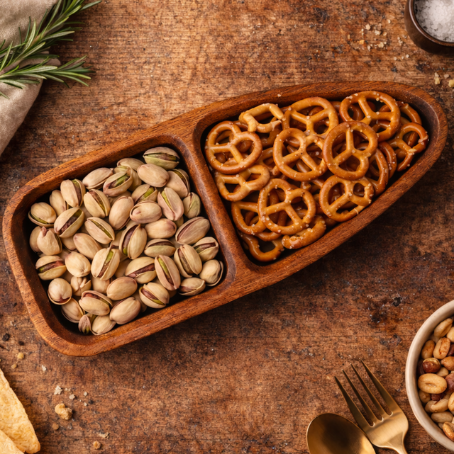 Wooden tray with pistachios and pretzels on a rustic wooden surface.