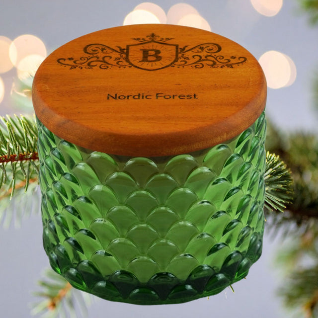 Green glass candle with wooden lid featuring 'Nordic Forest' on a blurred natural background