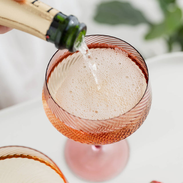 Champagne being poured into a pink glass with a blurred background