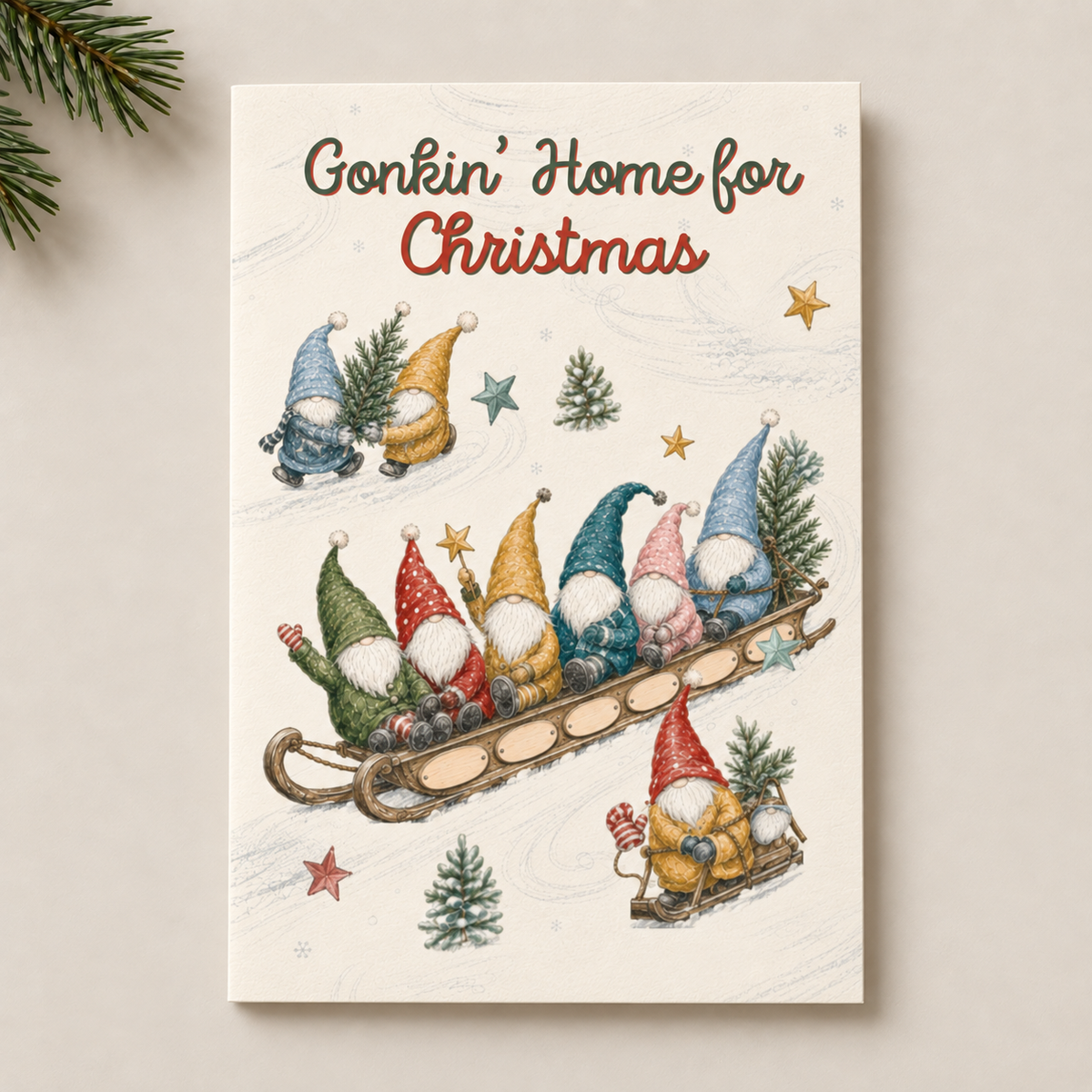A Christmas-themed art print or card featuring the text 'Gonkin' Home for Christmas' above a whimsical illustration of gnome characters in sleds, displayed against a light beige background with pine branches in the corner.