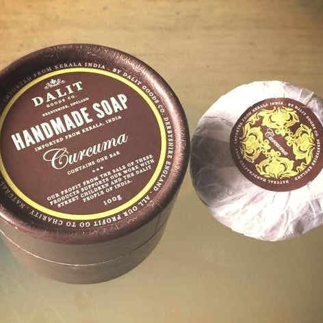 Handmade soap with a brown container and visible branding on a reflective surface.