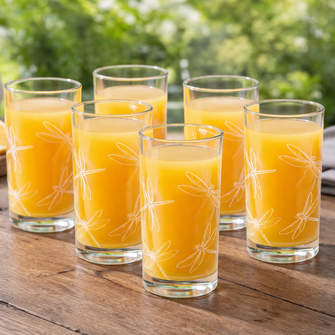 Six glasses of orange juice on a wooden table with oranges and a pitcher in the background.
