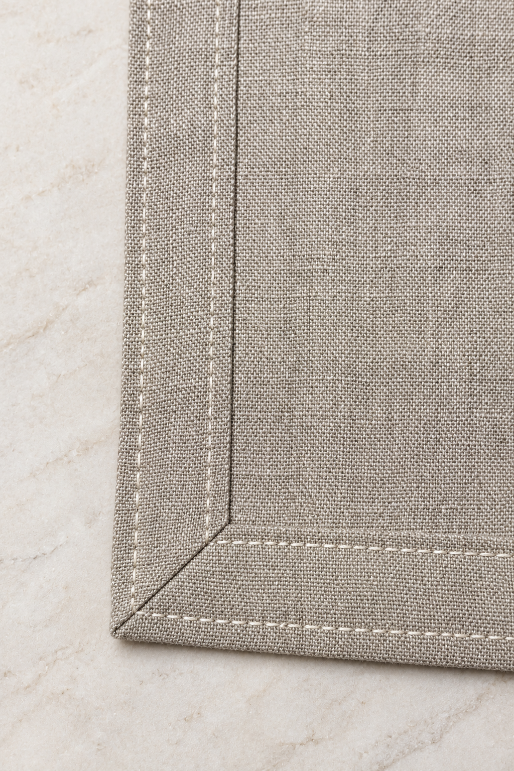 Close-up of a natural linen dragonfly napkin showing its mitred corner, double-fold hem and pale stitching.