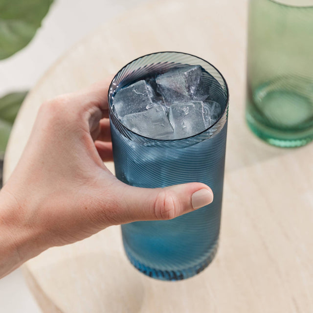 Hand holding a blue glass filled with ice cubes on a light surface.