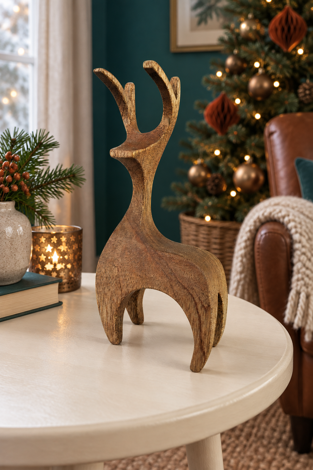 A rustic wooden reindeer figurine with a weathered brown finish stands on a round white table in a cozy, decorated living room with a Christmas tree in the background.
