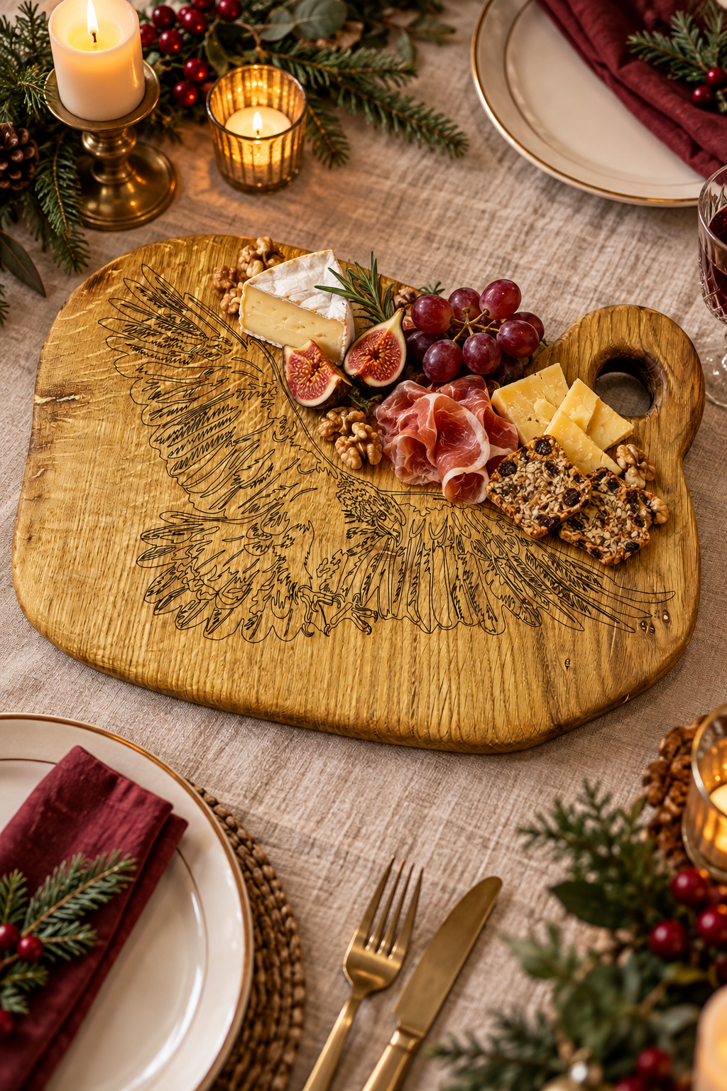 A rustic wooden charcuterie board with an engraved eagle design, styled on a table with cheese, crackers, grapes, figs, prosciutto, and candles in a holiday setting.
