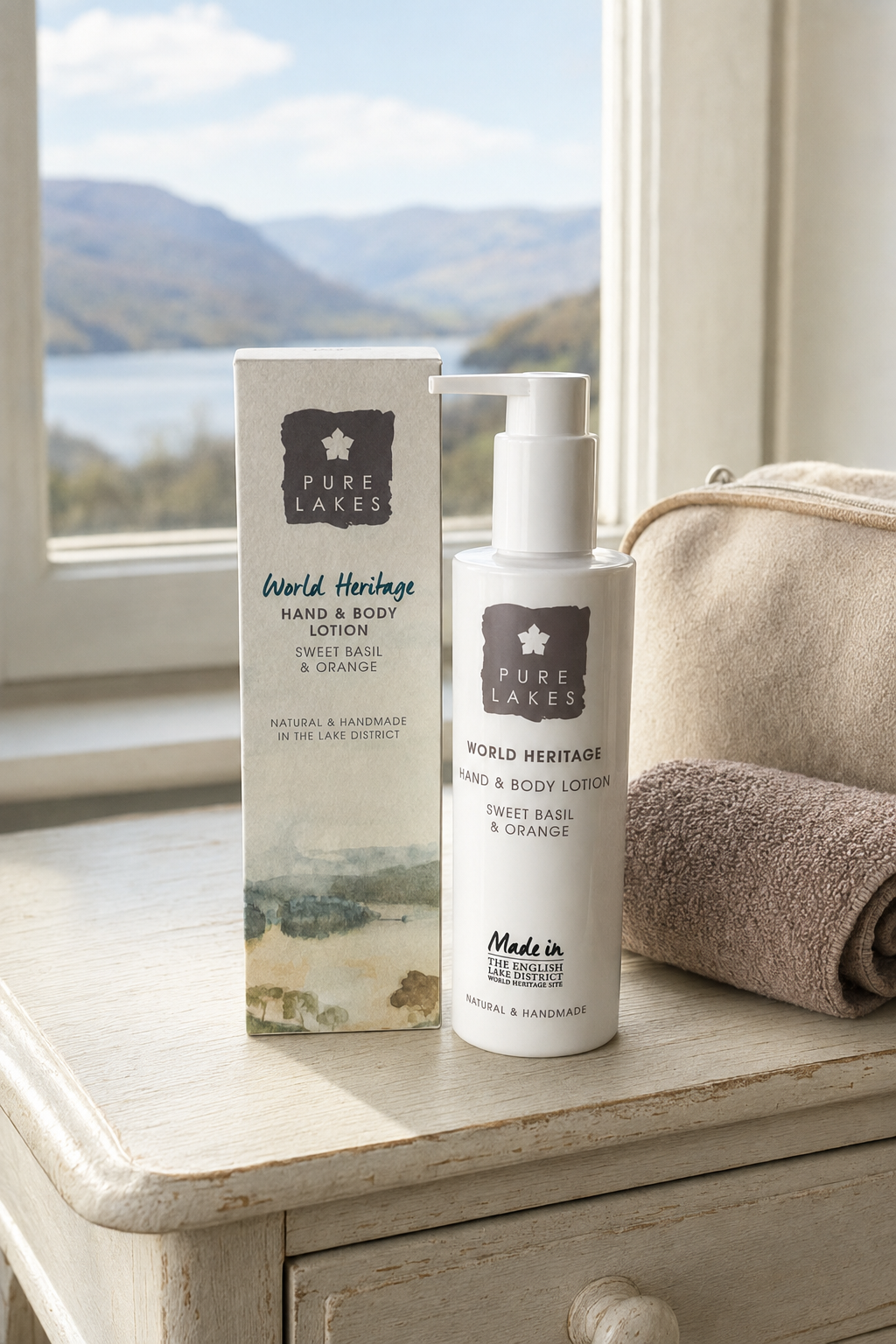 Pure Lakes World Heritage Sweet Basil & Orange Hand & Body Lotion bottle and its matching outer box, styled on a rustic white wooden table next to a beige towel, with a scenic lake and mountains in the background.
