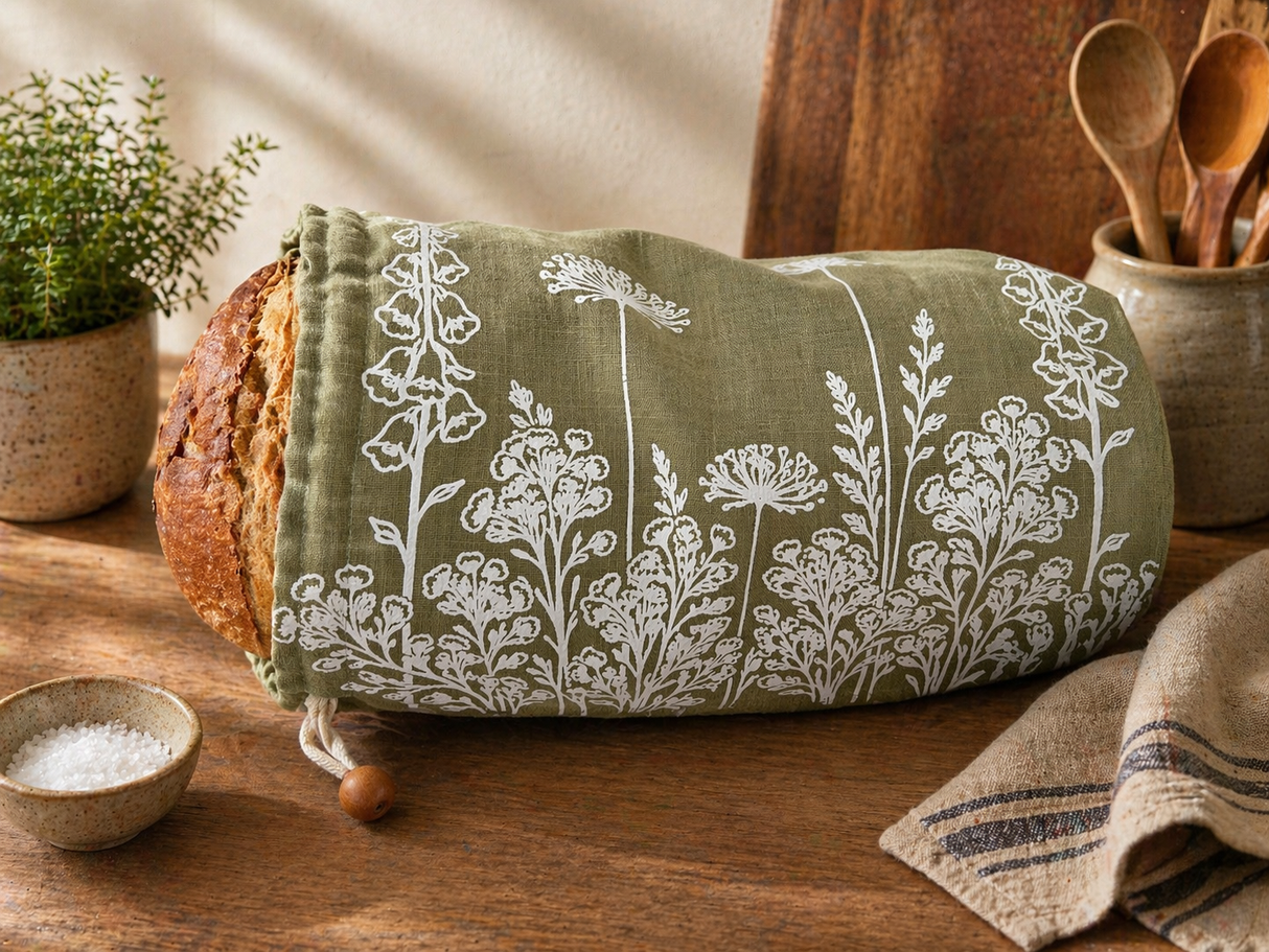 Loaf of bread wrapped in a green towel with white floral patterns on a wooden table.