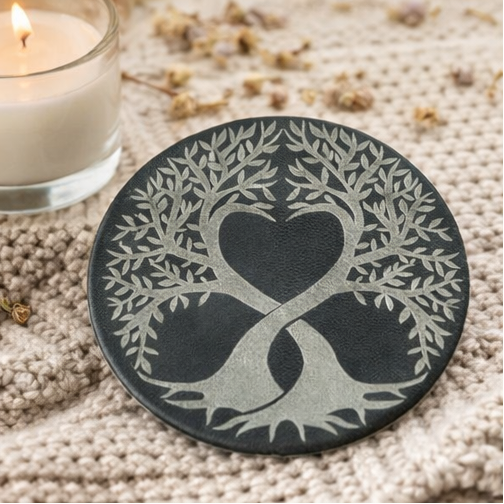 Set of four black leather coasters with tree-of-life design on a wooden surface.