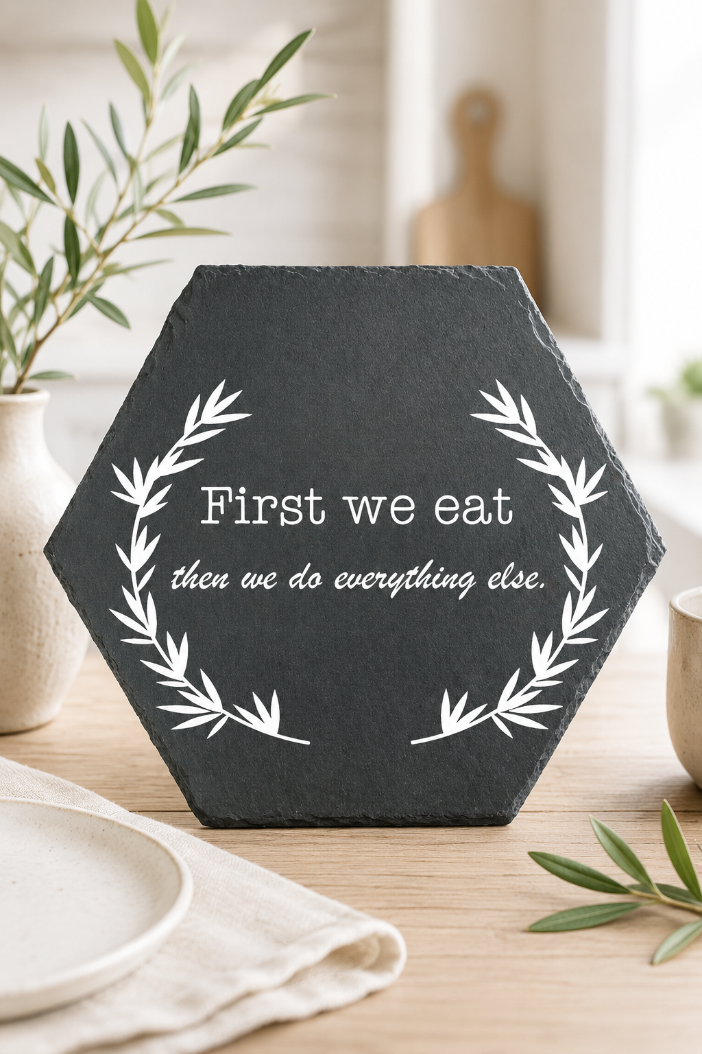 Hexagonal black slate with white text on a wooden surface with plants and plates in the background