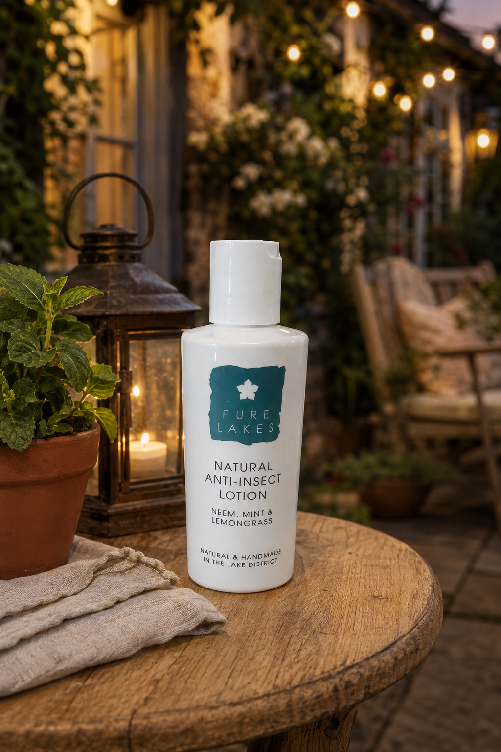 A bottle of Pure Laces Natural Anti-Insect Lotion sits on a rustic wooden table outdoors at dusk, surrounded by a lantern, potted plants, and warm string lights in the background.