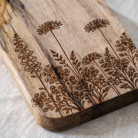 Wooden cutting board with floral engraved designs on a table setting.
