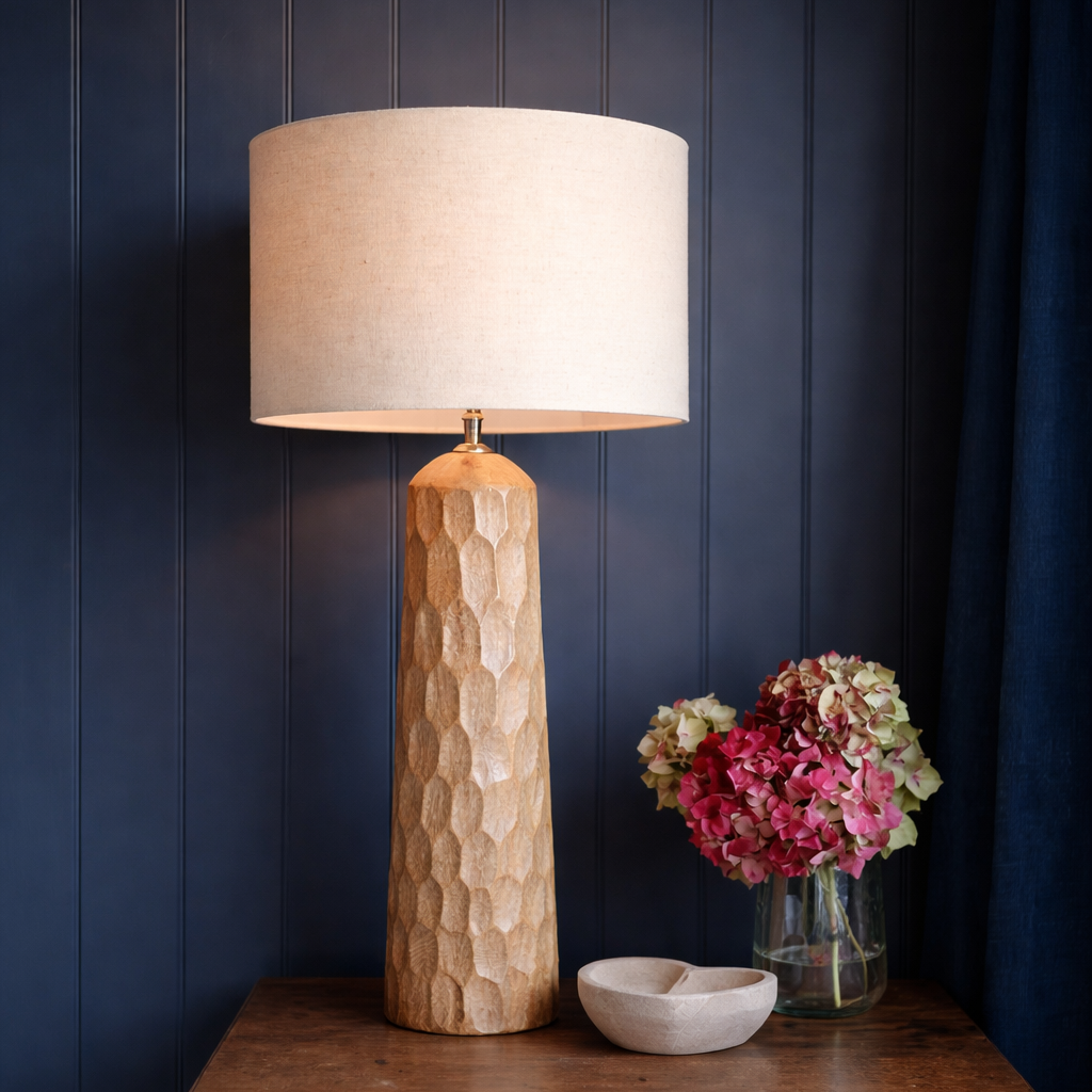 Table lamp with textured base on a wooden table against a dark blue wall
