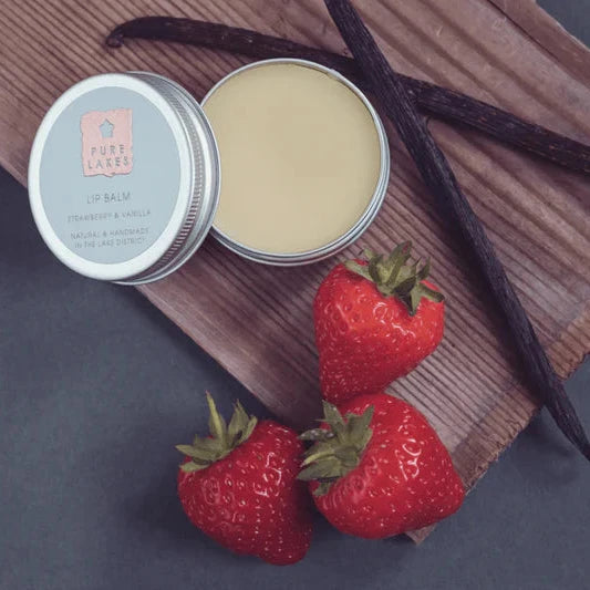 Tin of balm with strawberries and vanilla beans on a wooden board