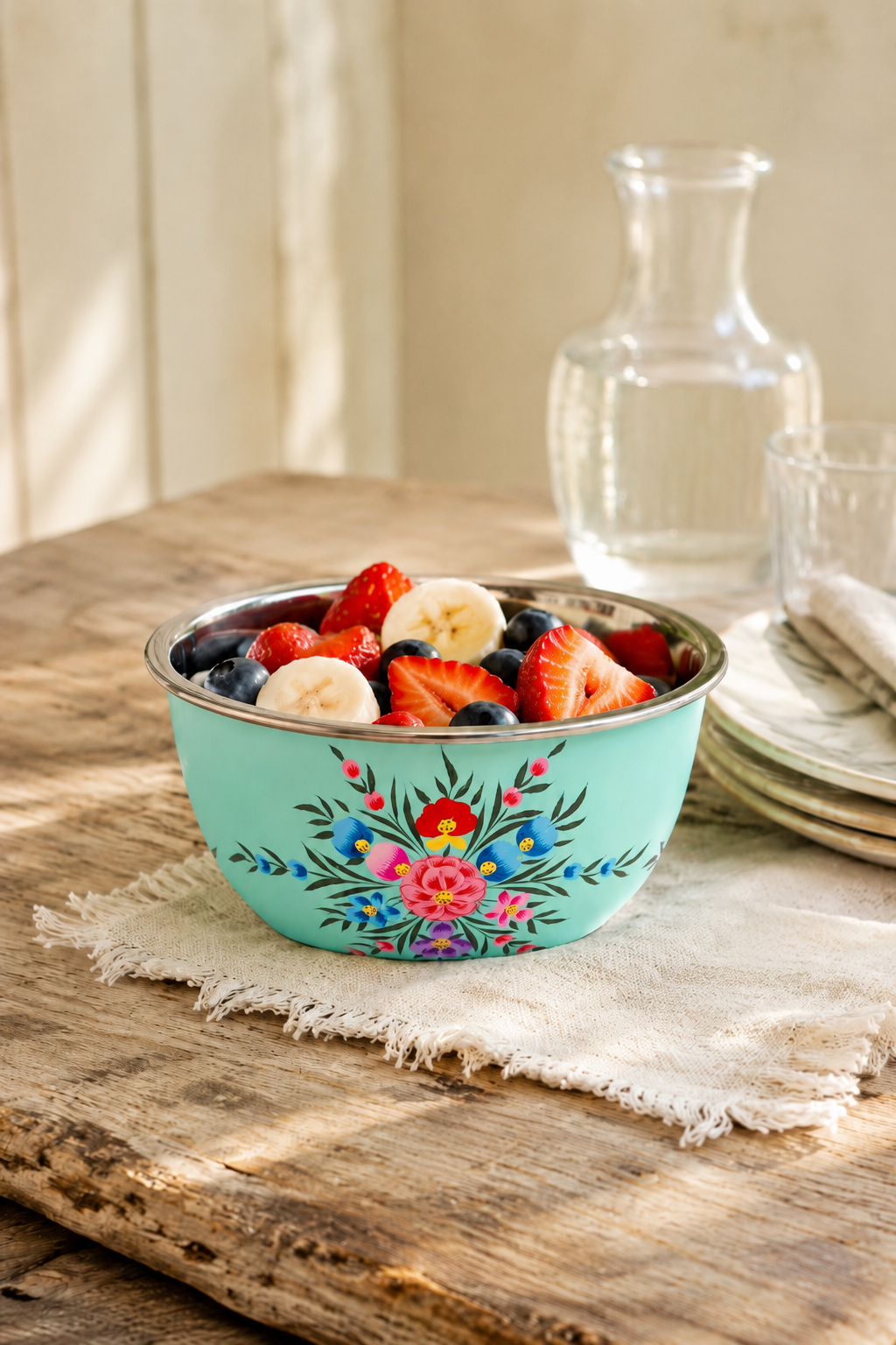 Turquoise bowl with floral design filled with fruit on a wooden table