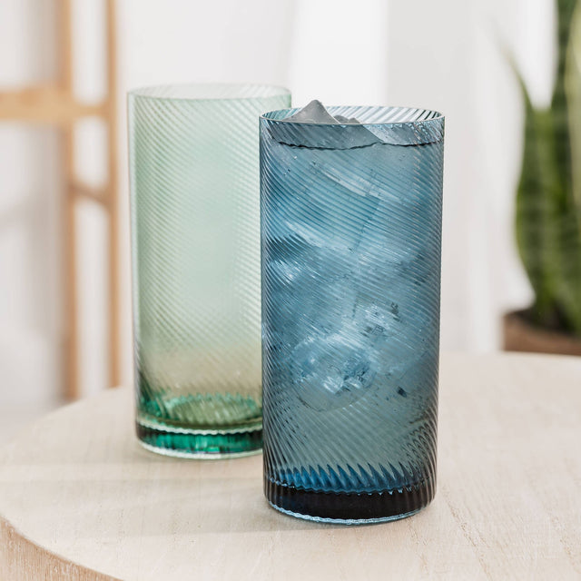 Two blue and green textured glass tumblers on a light surface with a blurred background