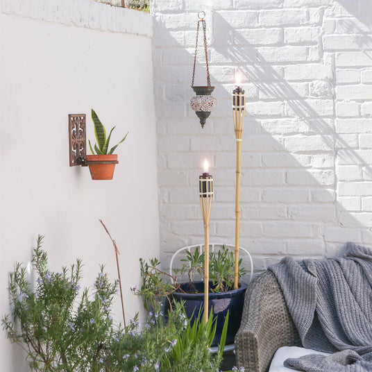 Outdoor setting with plants, a wall sconce, and decorative torches against a white brick wall.
