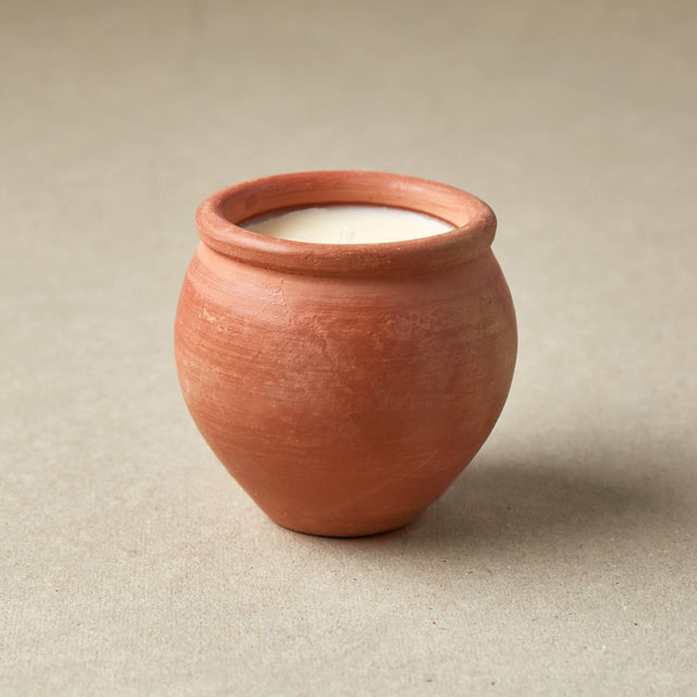 Terracotta pot with a white candle inside on a beige background