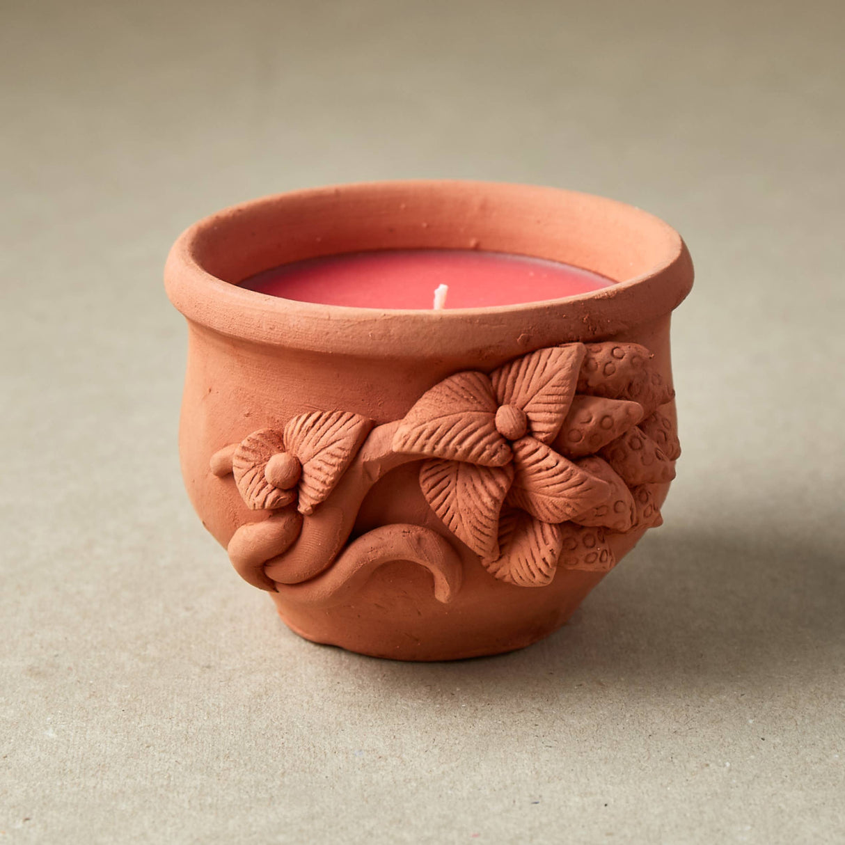 Terracotta candle holder with floral designs on a neutral background