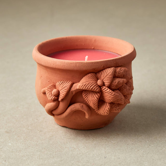 Terracotta candle holder with floral designs on a neutral background