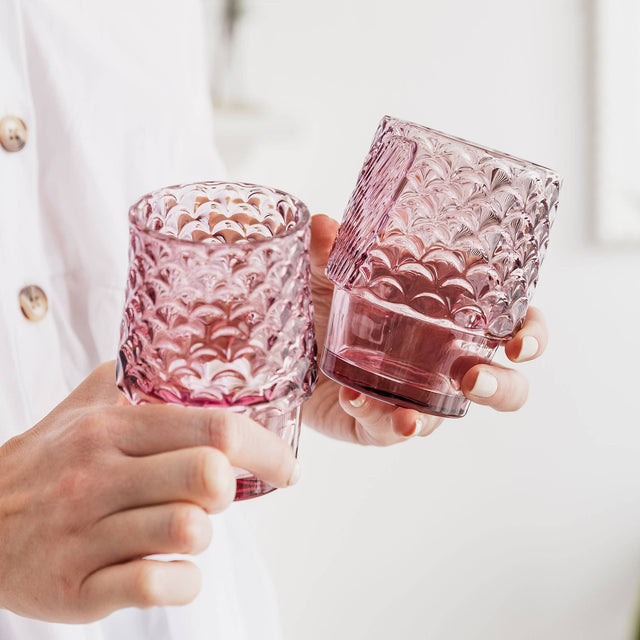Two hands holding pink textured glasses against a white background