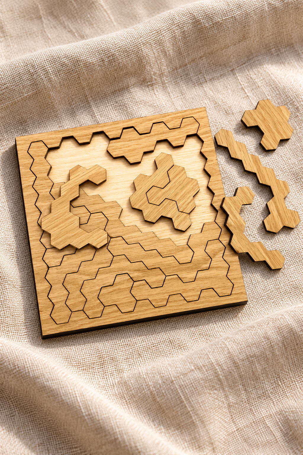 Close-up of the partly assembled square Hard Hex puzzle on linen, showing pale oak grain and intricate angular pieces.