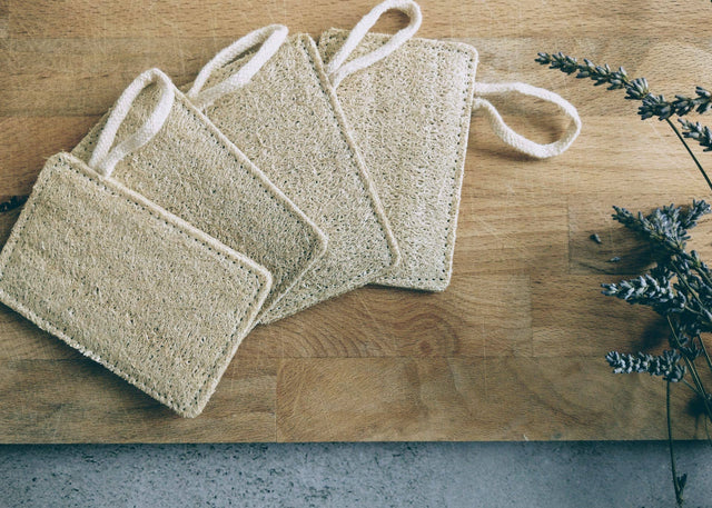 Three natural fiber scrubbies on a wooden surface with lavender flowers.