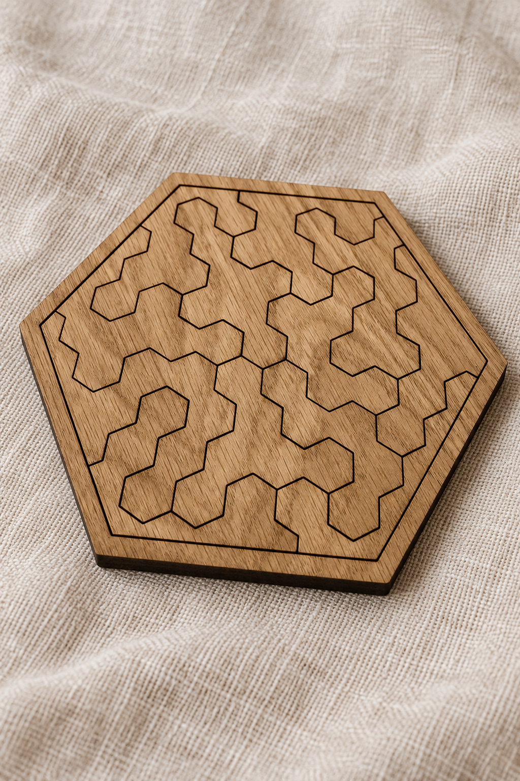 Close-up of the assembled Pocket Hex puzzle on linen, showing geometric pieces, oak veneer and a thin dark edge.