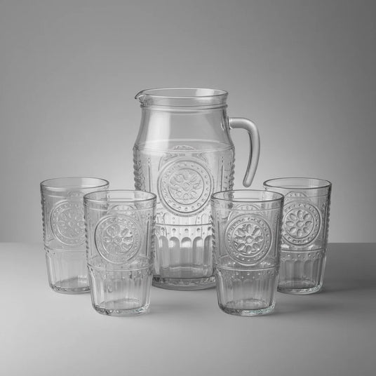 Set of clear glass pitcher and tumblers with embossed designs on a gray background