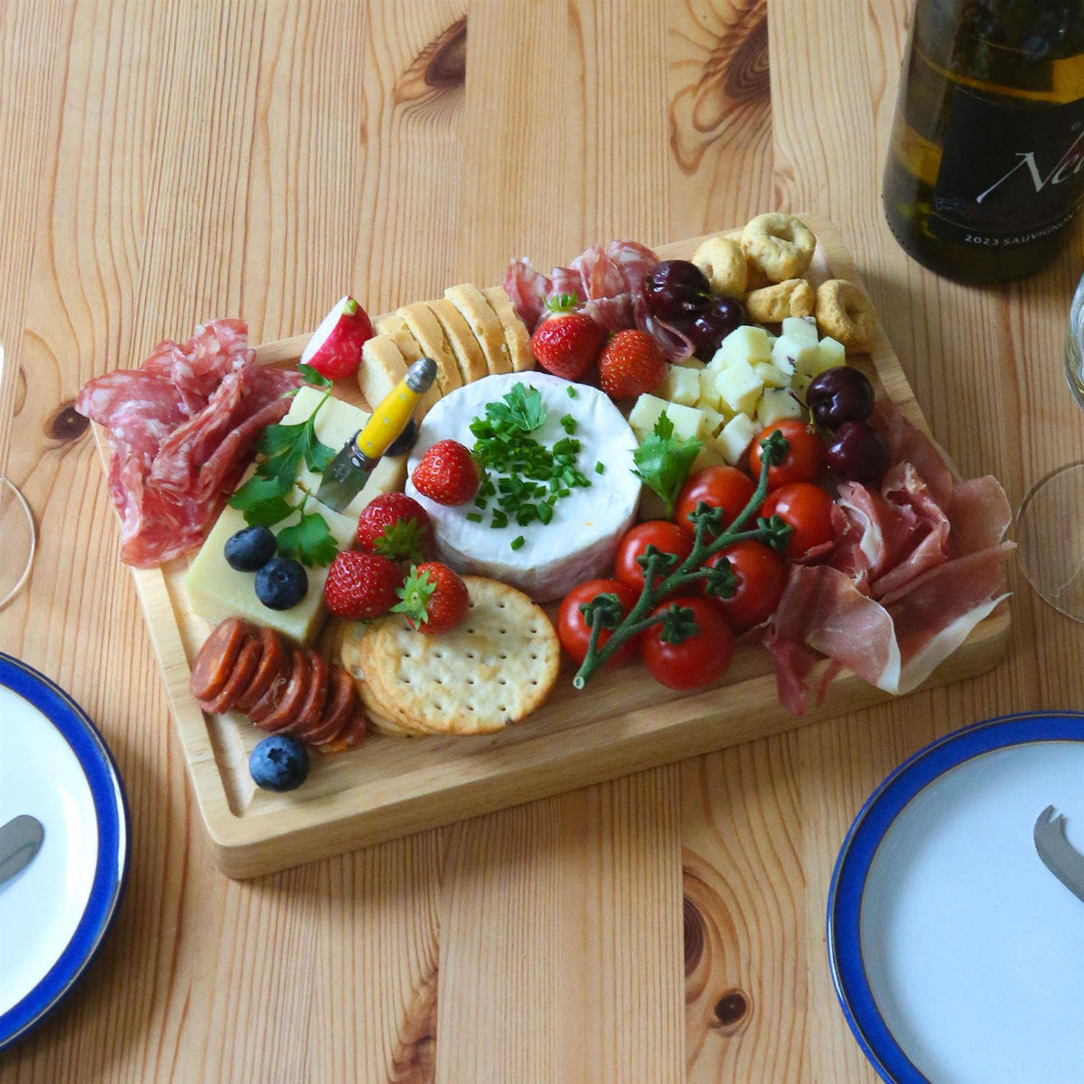 30 × 20cm rubberwood serving board filled with soft cheese, cured meats, crackers, berries, grapes and tomatoes on a wooden dining table.
